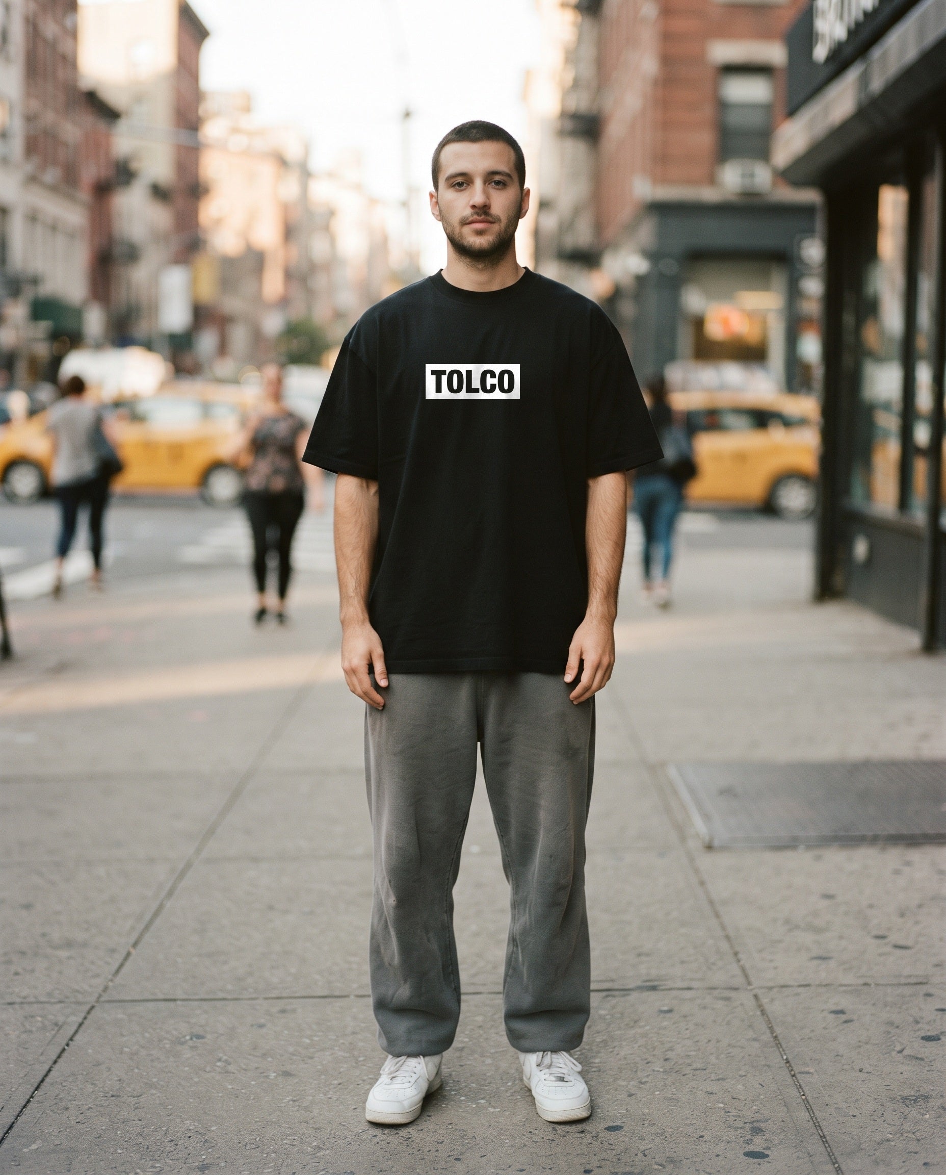 TOLCO on-model: TOLCO. - TAG - Pure Cotton T - Black, front view, worn on the street